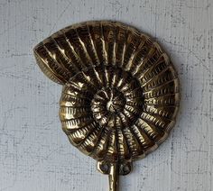 a gold metal wall hook on a white wall with an intricate fan shaped design hanging from it's side