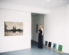 a woman standing in an empty room with paintings on the wall