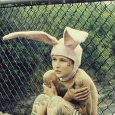 a woman with tattoos and bunny ears on her head sitting in front of a fence