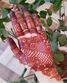 a hand with henna painted on it next to some green plants and greenery