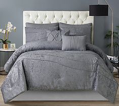 a bed with grey and white comforters in a bedroom next to a lamp on a table