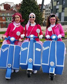 three women dressed in pink and blue are riding scooters