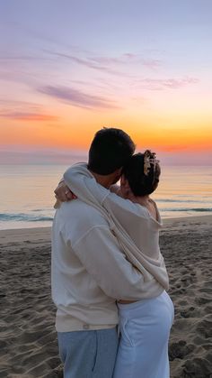 a man and woman hug on the beach at sunset