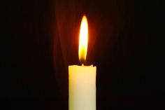 a lit candle in the dark with its light shining on it's side and black background