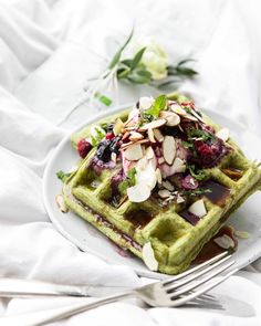 a white plate topped with green waffles covered in toppings and almonds