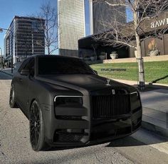 a black rolls royce parked on the side of a road in front of tall buildings