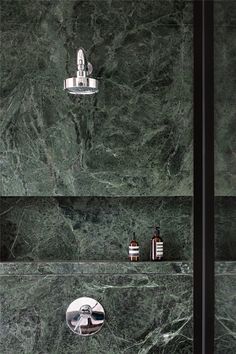 a green marble shower with chrome fixtures and soap dispensers on the wall