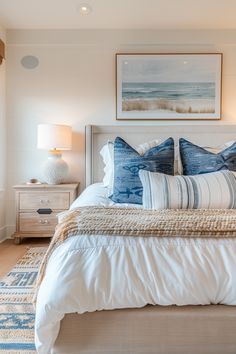 a bed with blue and white pillows on top of it next to a painting hanging above the headboard