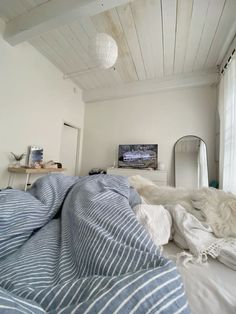 an unmade bed with blue and white striped comforter in front of a flat screen tv