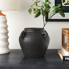 a black vase sitting on top of a table next to a lamp