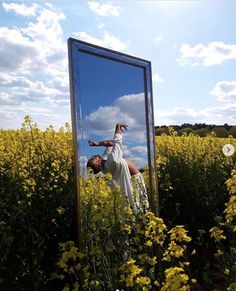 a woman standing in front of a mirror on top of a field of yellow flowers