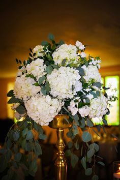 white flowers and greenery in a gold vase on a table at a wedding reception