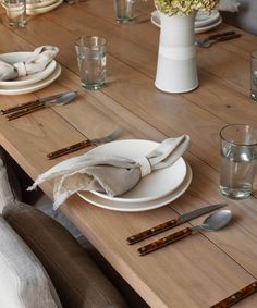 a wooden table topped with white plates and silverware