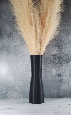 a tall black vase with some brown and white fur on it's side, against a gray background