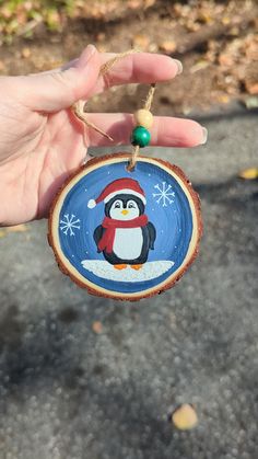 a hand holding a wooden ornament with a penguin on it