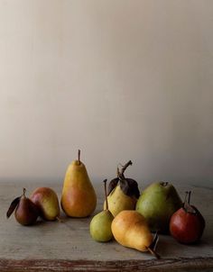 a group of pears and other fruit on a wooden table in front of a white wall