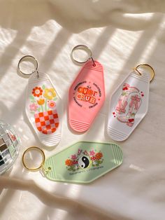 four keychains with different designs on them sitting on a white cloth covered surface