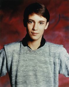 a young man wearing a sweater and posing for a photo in front of a red background