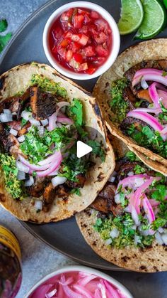 three tacos on a plate with salsa, onions and cilantro in the background