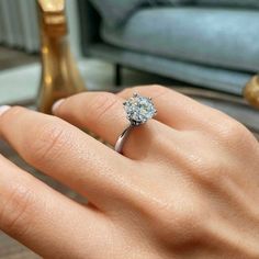 a woman's hand with a diamond ring on her finger, in front of a couch