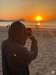 a person taking a photo on the beach with their cell phone at sunset or sunrise