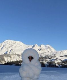 a snowman is standing in the snow with mountains in the background