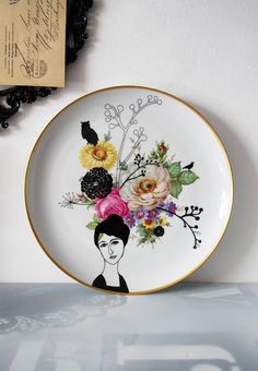 a plate with flowers painted on it sitting next to a black and white wall hanging