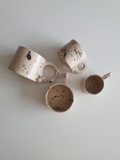 three cups and two spoons sitting on top of a white table next to each other