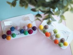 two pairs of earrings with pom - poms on them sitting next to each other