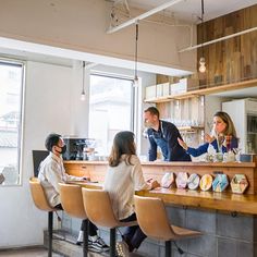 three people sitting at a counter in a coffee shop, one person is talking to the other