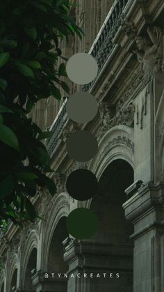 an old building with green and white circles hanging from it's ceiling, next to a tree