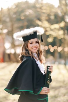 a woman wearing a graduation cap and gown holding a book in one hand while smiling at the camera