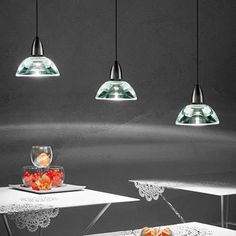 three lights are hanging from the ceiling above two tables with fruit on them and one is empty