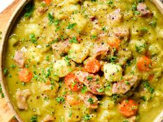 a bowl filled with meat and vegetable soup on top of a wooden table next to a spoon