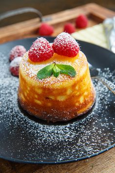 a dessert with raspberries and powdered sugar on top is sitting on a black plate