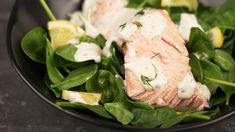 salmon and spinach salad with dressing in a black bowl on a counter top, ready to be eaten