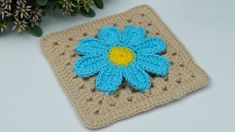 a crocheted square with a blue flower on it sitting next to some flowers