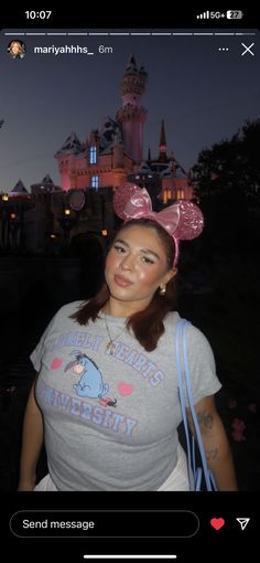 a woman wearing a pink minnie mouse ears hat in front of a castle at night