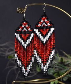 two red and white beaded earrings hanging from a hoop on a black background with greenery