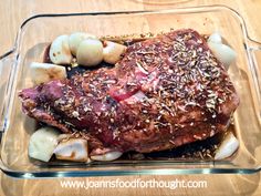 a glass dish filled with meat, potatoes and seasoning on top of a wooden table