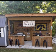 an outdoor bar and grill area with stools in the foreground, next to a shed