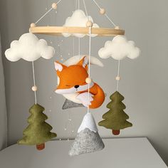 a stuffed fox hanging from a mobile with trees and snow on the ground in front of it