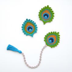 three crocheted peacock brooches with tassels and beads on a white background