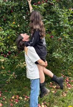 a boy and girl are in an apple orchard picking apples from the trees with their arms around each other