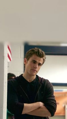 a young man leaning against a wall with his arms crossed