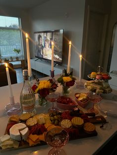 a table topped with lots of food and wine next to a flat screen t v