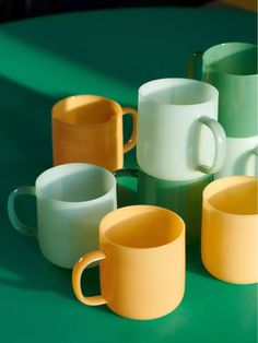 five different colored coffee mugs on a green surface