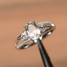 a ring with an oval cut stone surrounded by small white diamonds on a wooden surface