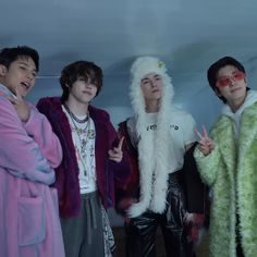 four young men standing next to each other wearing furry coats and holding peace signs in their hands