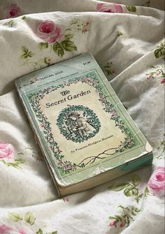 a book laying on top of a bed covered in pink roses and white linens